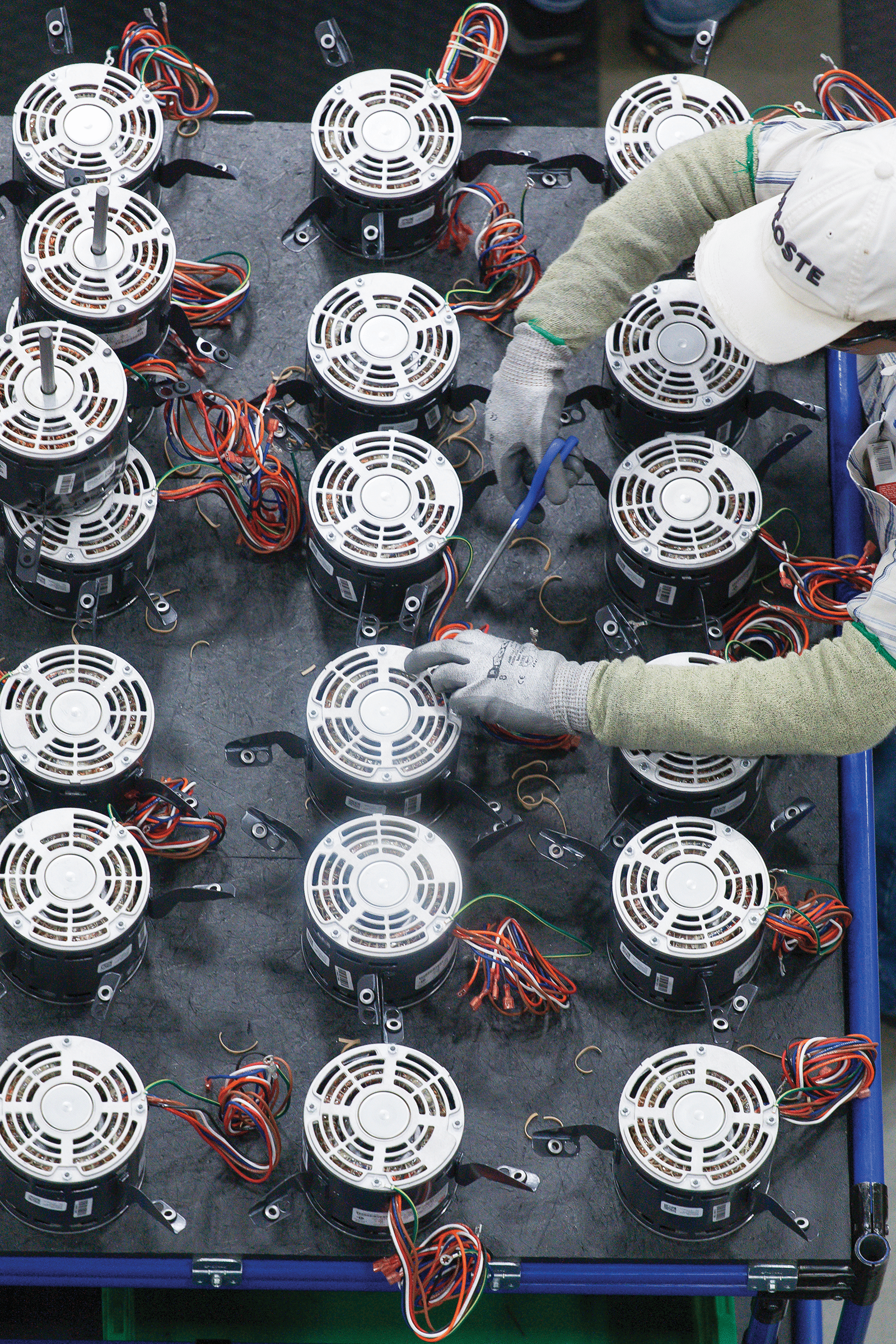 A man works at a table surrounded by several Amana Blowers, focusing on a task involving the fans.