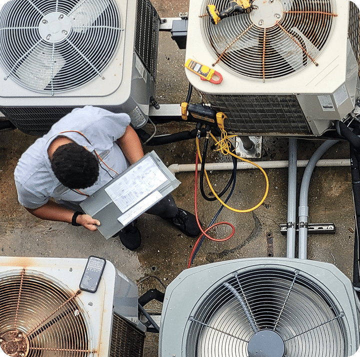 A man stands beside a large air conditioner, inspecting the unit outdoors for maintenance or repair.