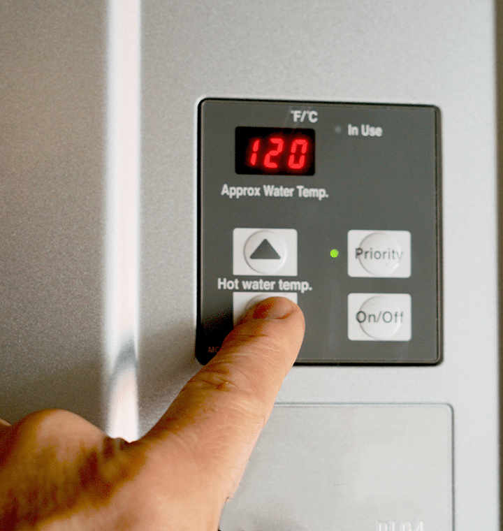Person adjusting the thermostat button to set the water tank temperature.