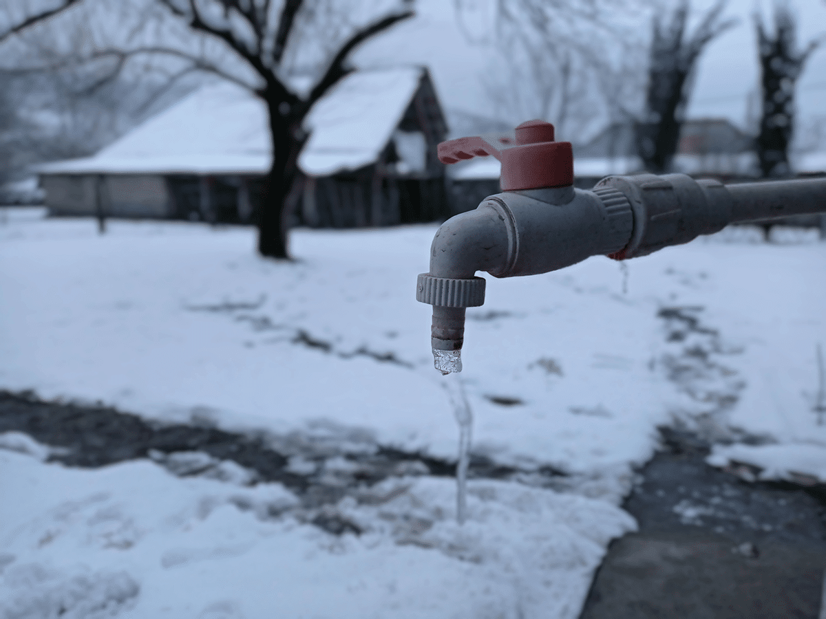 A water faucet with a red valve, partially buried in snow, illustrating a frozen faucet in a winter setting.