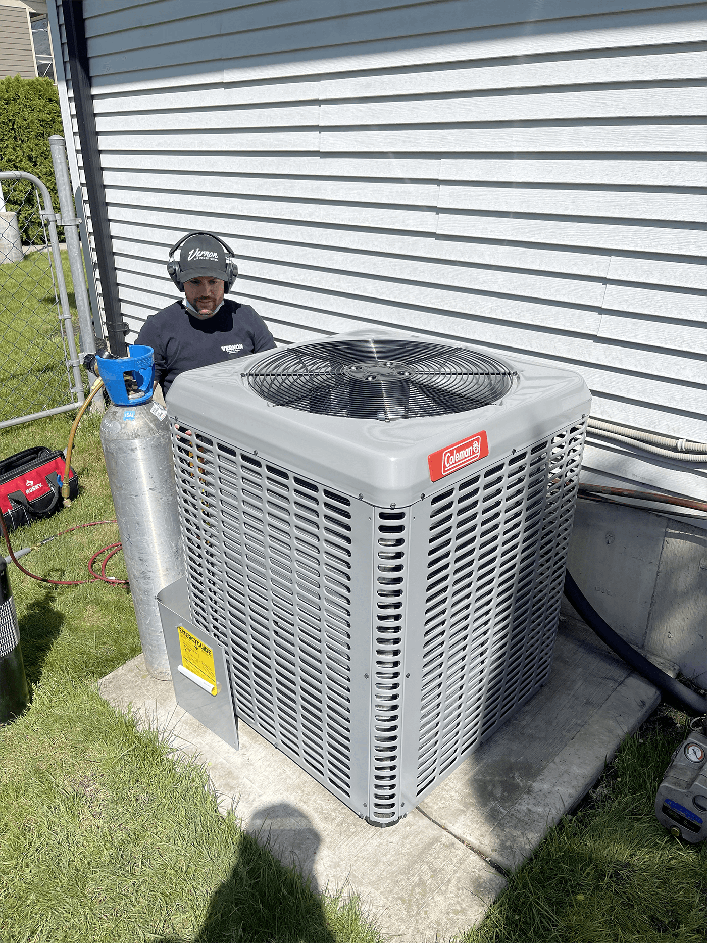 A man repairs a gray heat pump in front of a house, focusing on the AC system's maintenance.