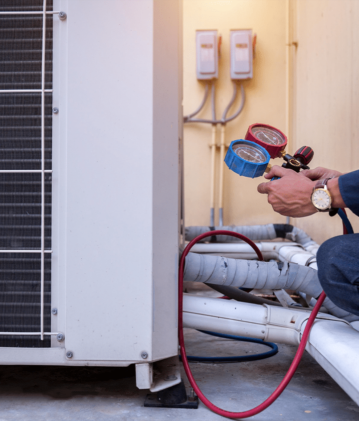 A man checks refrigerant pressure on an air conditioner using a hose during installation outside.