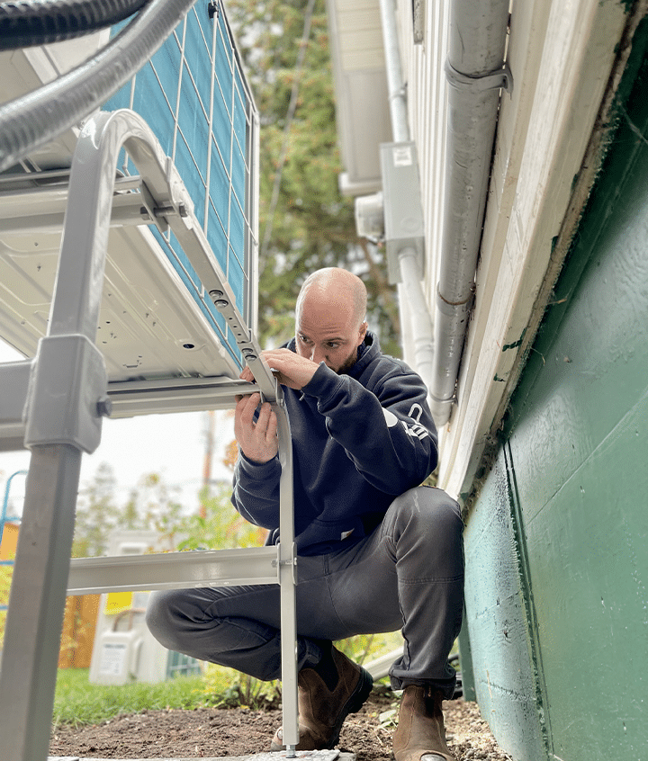 A man kneels to adjust a ladder against a house, showcasing his focus on home maintenance.
