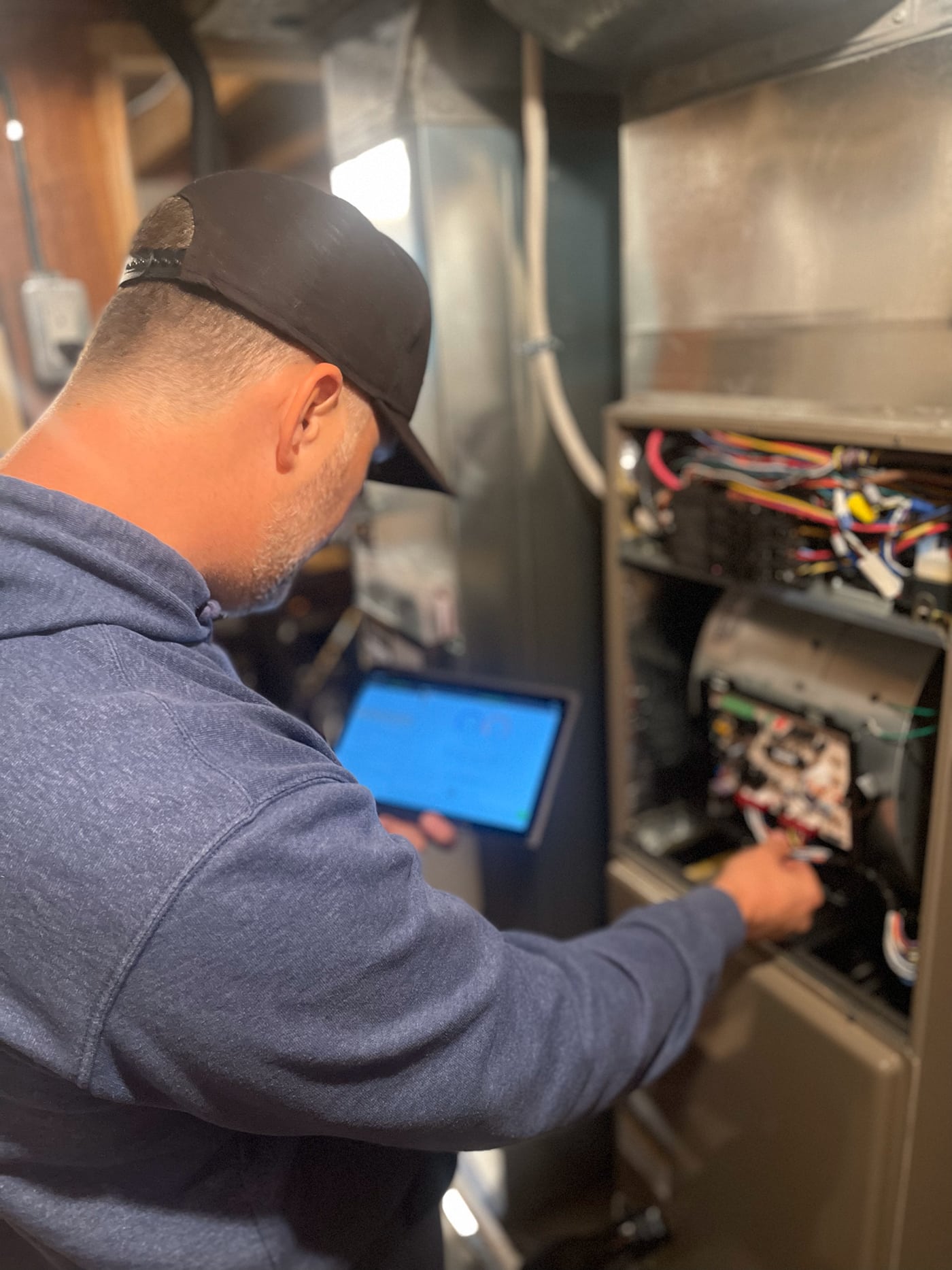 A technician inspects a furnace while using a tablet in a dimly lit utility room.