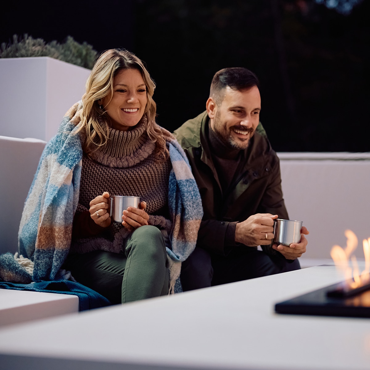 Happy woman and her husband enjoying by fireplace on a patio.